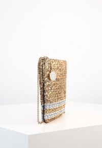 Kultainen paljettiraha, jossa on hopeinen raidoitettu yksityiskohta, varustettuna ketjuolkaimella ja pyöreällä logotarralla. Raskaampi pinta ja litteä muotoilu.