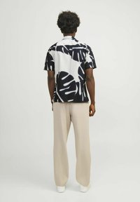 Camicia a maniche corte con bottoni, con motivo a foglie in bianco e nero, abbinata a pantaloni larghi beige chiaro e sneakers bianche.
