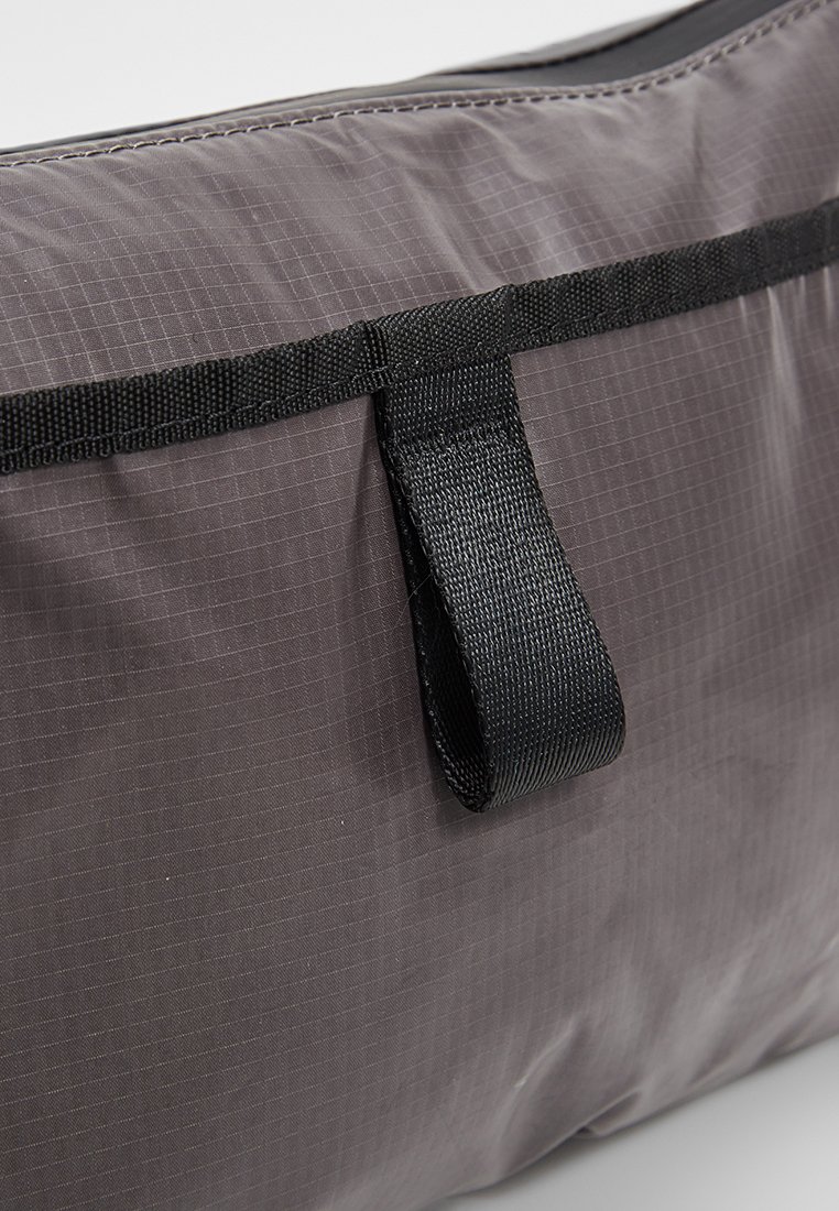 Grau gefärbte Stofftasche mit einer strukturierten Oberfläche im Rautenmuster, ergänzt durch einen schwarzen Gurt für eine einfache Handhabung.