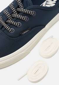 Tengerész kék vászon sneaker, texturált felső résszel, fehér gumitalppal �és fekete-fehér mintás fűzőkkel. Két pár fehér fűzőt tartalmaz.