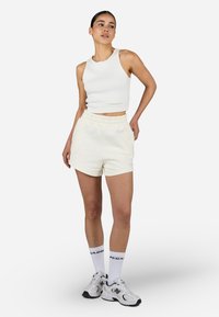 Biely rebrovaný crop top s okrúhlym výstrihom, v kombinácii so svetlo krémovými šortkami s elastickým pásom. Doplnil ho biely ponožky a tenisky.