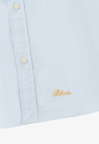 Hellblaues Button-Up-Hemd aus weichem Stoff. Mit cremefarbenen Knöpfen und gesticktem "Blk" in Orange auf der linken Seite.
