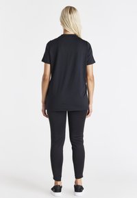 Černý krátký rukáv top s volným střihem, doplněný o přiléhavé černé kalhoty. Hladká textura, jednoduchý design, žádné viditelné vzory ani akcenty.