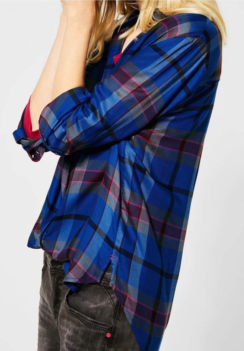 Blue and black plaid shirt with rolled-up sleeves; features a vibrant, checkered pattern in varying shades and a slightly curved hem.