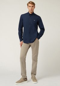 Marinel blauwe overhem shirt met een kraag, slim fit, gecombineerd met beige broeken en tan sneakers met een gestructureerd patroon en witte zolen.