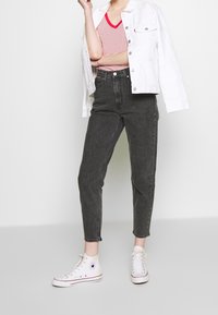 Jeans negros de tiro alto, diseño de pierna recta, combinados con una camisa de manga corta a rayas rojas y una chaqueta de mezclilla blanca. Zapatillas blancas completan el look.