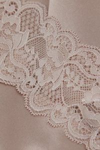 Zachtroze satijnen stof met een verfijnde kanten rand met bloemmotieven en delicate details langs de rand. Gelaagd en gestructureerd ontwerp.