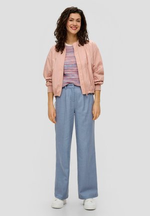 Veste bomber rose clair sur un haut en maille multicolore, associée à un pantalon large bleu clair et des baskets blanches. Coupe standard, design décontracté.