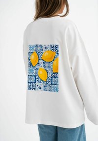 Witte sweatshirt van zachte stof met een blauwpatroon vierkant met vier gele citroenen op de achterkant. Casual pasvorm en ronde halslijn.