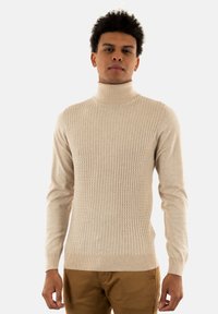 Maglione collo alto a coste beige con maniche lunghe, realizzato in un morbido materiale a maglia; presenta una vestibilità aderente e un motivo testurizzato.