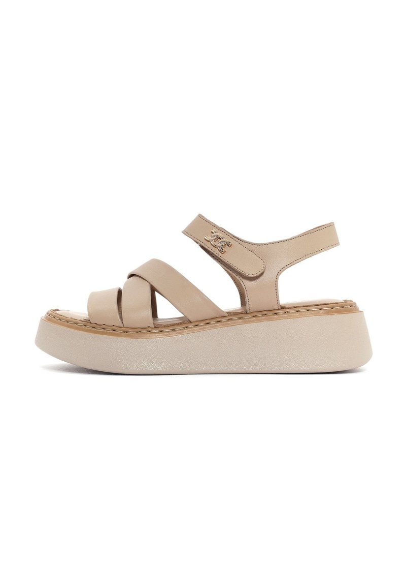 Sandali platform color beige chiaro con cinturini incrociati, una suola spessa e testurizzata, e un cinturino alla caviglia sicuro con discrete minuterie dorate.