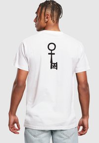 Hvid bomulds T-shirt med et stort sort grafisk design på ryggen, der ligner en nøgle og et kønssymbol. Casual pasform med korte ærmer.