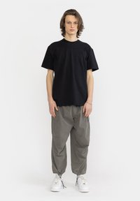 Zwarte katoenen t-shirt met korte mouwen, gecombineerd met olijfgroene cargobroeken met zakken, elastische manchetten en witte sneakers.