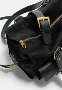 Sac noir en matériau doux avec une fermeture éclair dorée, des accents en cuir noir et une bandoulière réglable. Dispose d'un rabat sur le dessus et de détails en métal.