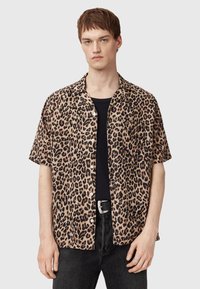Korthylset, leopardmønstret skjorte i beige og sort med en afslappet pasform, knaplukning og en enkelt brystlomme, parret med mørke jeans.