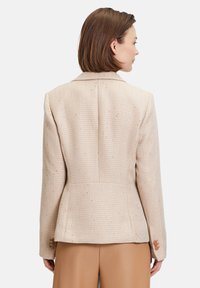 Blazer beige a spina di pesce con una vestibilità strutturata, chiusura con un bottone e una texture sottile. Presenta un colletto a punta e maniche sartoriali.