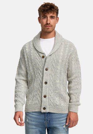 Kabelstickad cardigan i ljusgrått med en sjalkrage, fem bruna knappar samt ribbade muddar och våll. Jeans i denim med slitna detaljer.