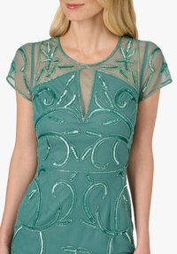 Turkusowa sukienka z przezroczystymi, krótkimi rękawami, ozdobiona misternymi koralikami i kwiatowymi wzorami. Posiada dopasowany gorset z dekoltem w kształcie litery V.