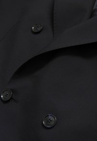 Czarna tkanina o gładkiej fakturze, z dwoma czarnymi guzikami i detalem w postaci ostrych kołnierzyków, podkreślająca proste linie i minimalistyczny design.