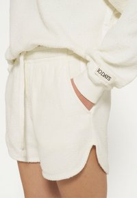 Shorts in tessuto di spugna bianco con vita regolabile tramite cordino, tasche laterali e polsini a costine. Presentano un orlo arrotondato e un'etichetta "10 DAYS".