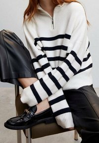 Weißer und marineblauer gestreifter Pullover mit Viertelreißverschluss, gerippter Struktur, kombiniert mit schwarzen Lederhosen und glänzenden schwarzen Slippern.