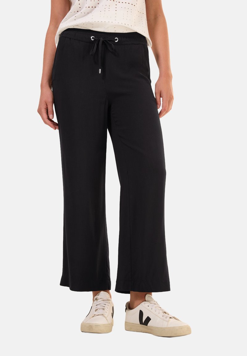 Pantalons larges noirs en tissu doux avec une taille élastique et un cordon de serrage. Associés à des baskets blanches avec des accents noirs.