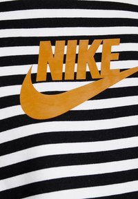 Svartvitt randigt tyg med en orange bold "NIKE"-logotyp och swoosh i en blank finish. Slät textur, avslappnad design.