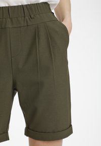 Pantaloni corti verde oliva con una vita alta elasticizzata, caratterizzati da pieghe frontali, tasche laterali e risvolti per un look raffinato.