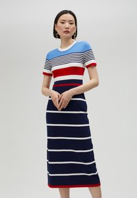 Randig klänning med blå, röda och vita horisontella ränder. Korta ärmar, rund halsringning och en figursydd siluett med knälång nederdel.