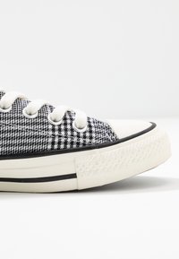 Baskets en toile à motif pied-de-poule noir et blanc, avec lacets blancs et semelle en caoutchouc. Dotées d'un bord noir et d'un bout texturé.