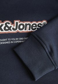 Granatowa bluza z ribbami na mankietach i dużym nadrukowanym logo w kontrastujących kolorach, w tym "Jack & Jones" oraz dodatkowym tekstem poniżej.