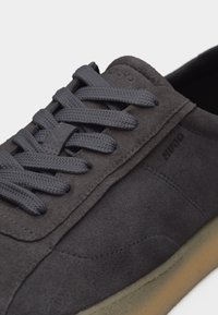 Baskets en daim gris foncé avec lacets assortis, nom de la marque embossé sur le côté et semelle en caoutchouc marron clair.