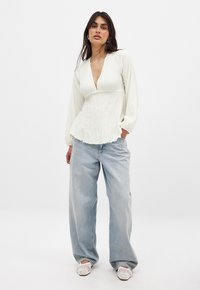Witte gemêleerde lange mouwen top met een diepe V-hals, peplum zoom, gedragen met lichtblauwe high-waisted wijd-uitlopende jeans en geweven witte schoenen.