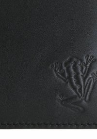 Surface noire texturée avec un contour de grenouille en relief et des coutures visibles le long du bord inférieur.