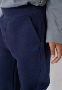 Navyblauwe sweatpants van zachte stof, met een zijzak en een gestikte logo in bijpassend blauw. Elastische tailleband voor comfort.