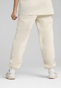 Cream-colored sweatpants with a loose fit, elastic cuffs, and a smooth cotton texture, paired with white sneakers featuring beige accents.