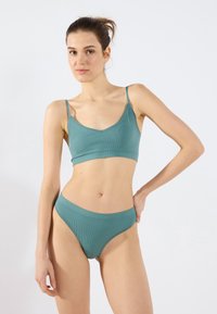 Teal ribbed bralette with adjustable straps and matching high-waisted bikini. Both feature a subtle lace trim along the edges.