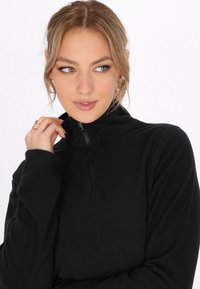 Zwarte fleece trui met een hoge nek en rits, met lange mouwen en een zachte textuur. Eenvoudig ontwerp, geschikt voor lagen.