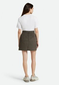 Gonna mini in lana marrone con vita aderente, cerniera sul retro e pieghe sottili. Abbinata a una t-shirt bianca semplice e sneakers chiare.