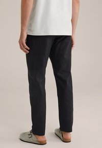 Fekete, keskeny, pamut anyagból készült nadrág, szürke slip-on cipővel párosítva. Az öltözet egyszerű, hétköznapi megjelenésű.