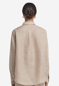 Beige langærmet skjorte, tekstureret stof, afslappet pasform, rygfold, klassisk krave, knapmanchetter, vist bagfra.