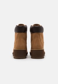 Bottes en cuir marron avec une tige haute, dotées d'un col rembourré noir, d'une semelle épaisse marron et de surpiqûres décoratives sur les côtés.