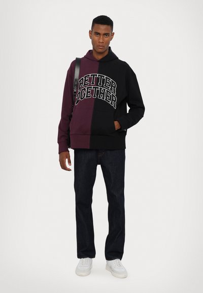 Hoodie noir et bourgogne à blocs de couleur avec le texte "MIEUX ENSEMBLE," associé à un jean sombre et des baskets blanches.