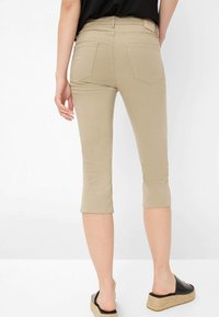 Pantalons beige cropped avec une coupe slim, fabriqués dans un tissu doux, taille mi-haute et deux poches arrière. Associés à des sandales à plateforme noires.