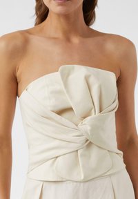 Góra bez ramiączek w kolorze kremowym z designem w formie skręconego węzła, wykonana z gładkiego materiału. Posiada wyraźne szwy i dopasowany krój.