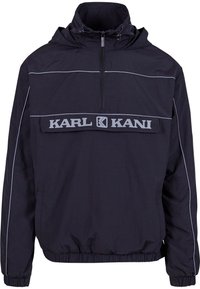 Black hooded windbreaker jacket with front zipper, elastic cuffs, and "KARL KANI" logo across chest on a flap pocket.