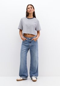 Pruhovaný crop top s námořnickým límcem, spárovaný s širokými světle modrými džíny. Oblečení má volný střih a pohodlné tenisky.