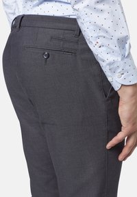 Grå skräddarsydda byxor i texturerat tyg, med en bakficka med knäppning och sydda detaljer, bärs med en mönstrad skjorta.