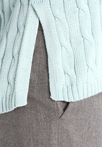 Mintgrön stickad tröja med ett flätat mönster, med sidosprund, kombinerad med grå strukturerade byxor.