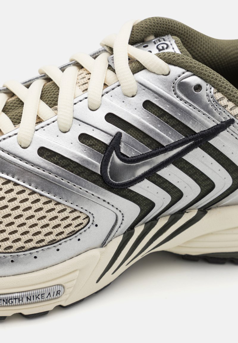 Nike-Sneaker mit einem Obermaterial aus Silber und Olivgrün, Netzpanel, cremefarbenden Schnürsenkeln, schwarzem Logo und einer strukturierten Sohle für besseren Grip.